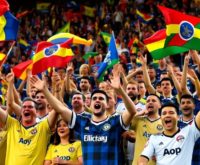 Excited soccer fans in jerseys at a stadium.