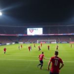 Soccer players in action under bright stadium lights at night.